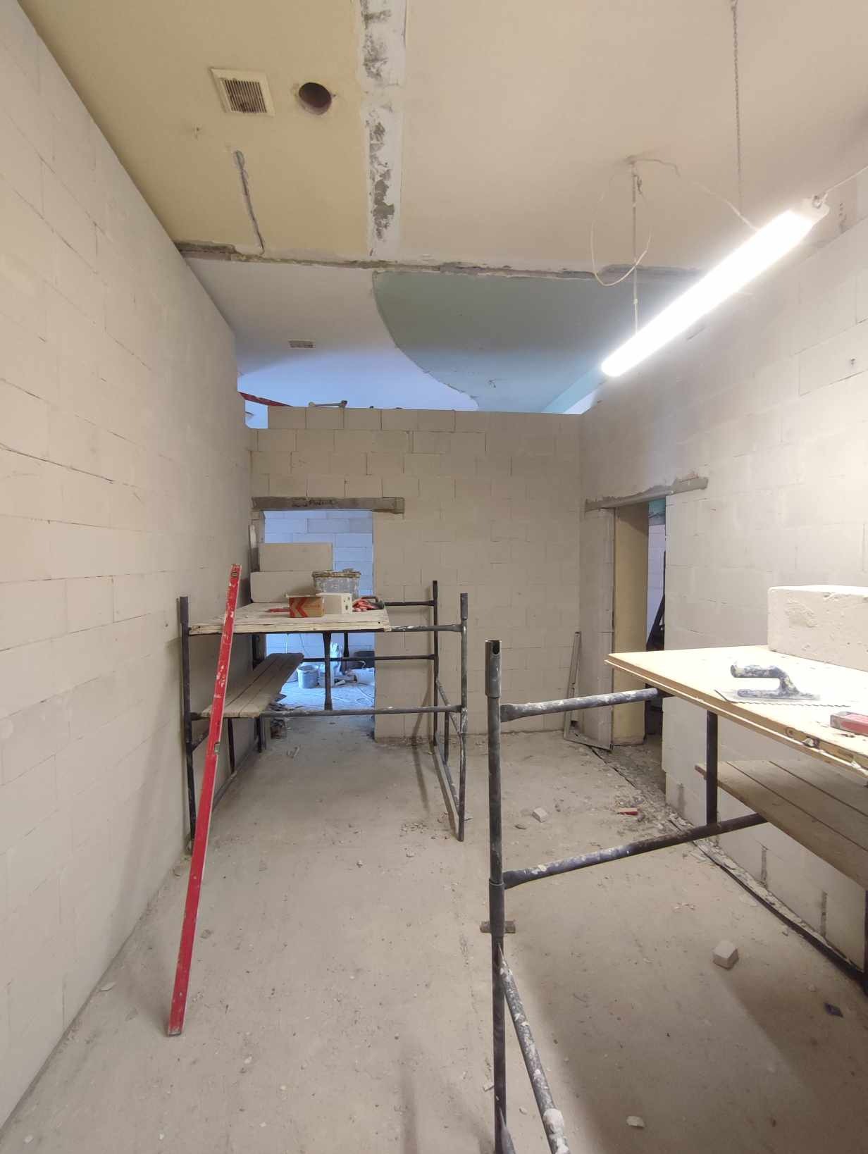 Wnętrze w trakcie remontu: ściany z białych bloczków, rozstawione rusztowania, widoczne narzędzia murarskie, surowy beton na podłodze.