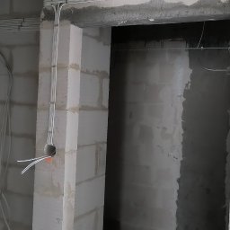 Dominik Gołębiewski - Instalacja elektryczna w surowym wnętrzu: kable prowadzone w listwach na ścianach z betonu komórkowego, widoczne przewody wychodzące z otworu w ścianie.