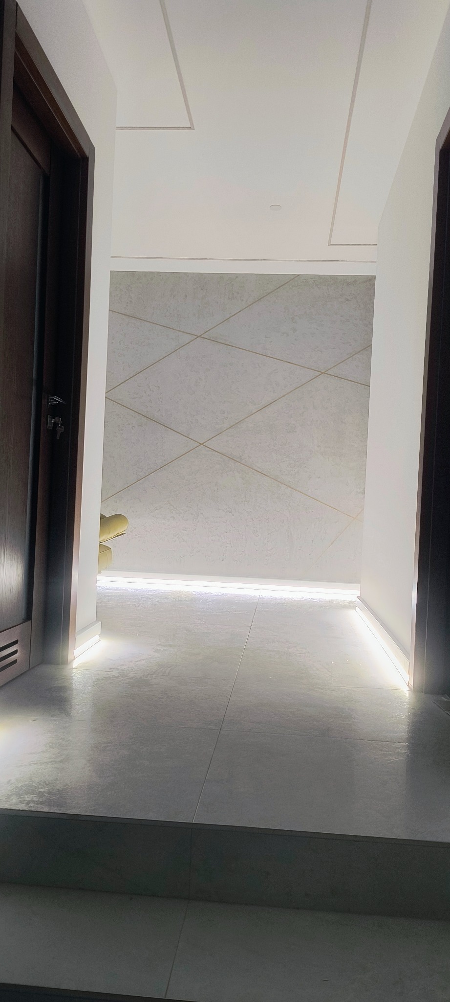 Nowoczesny korytarz z podświetleniem LED przy podłodze, widok z progu. Minimalistyczny design, jasne płytki i geometryczny wzór na ścianie. Drzwi po bokach kadru.