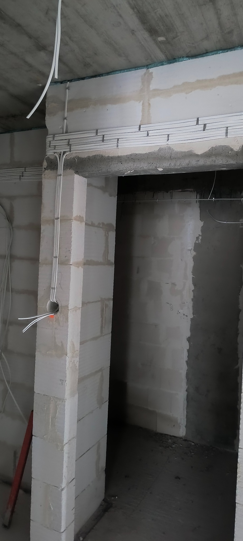 Instalacja elektryczna w surowym wnętrzu: kable prowadzone w listwach na ścianach z betonu komórkowego, widoczne przewody wychodzące z otworu w ścianie.