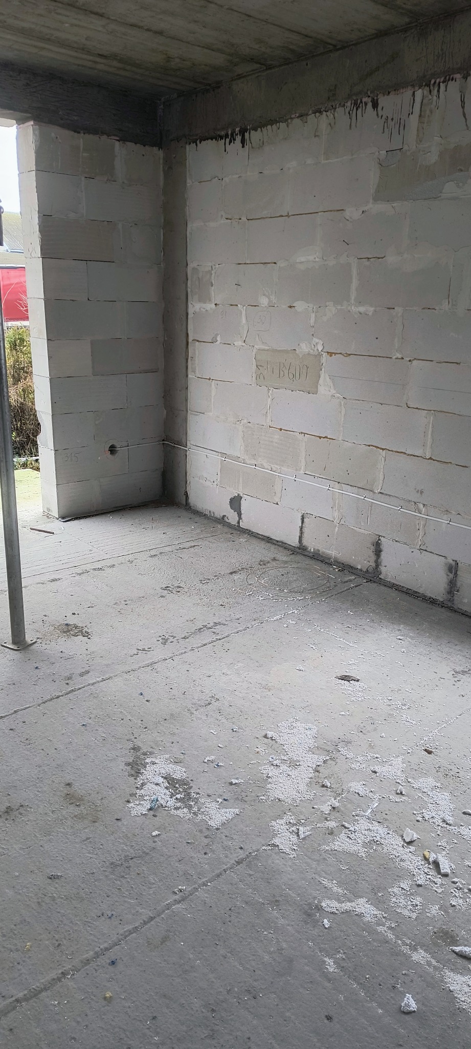 Surowy stan budynku w trakcie budowy z widocznymi przewodami elektrycznymi w ścianie z betonu komórkowego. Widoczne ślady po pracach budowlanych na podłodze.