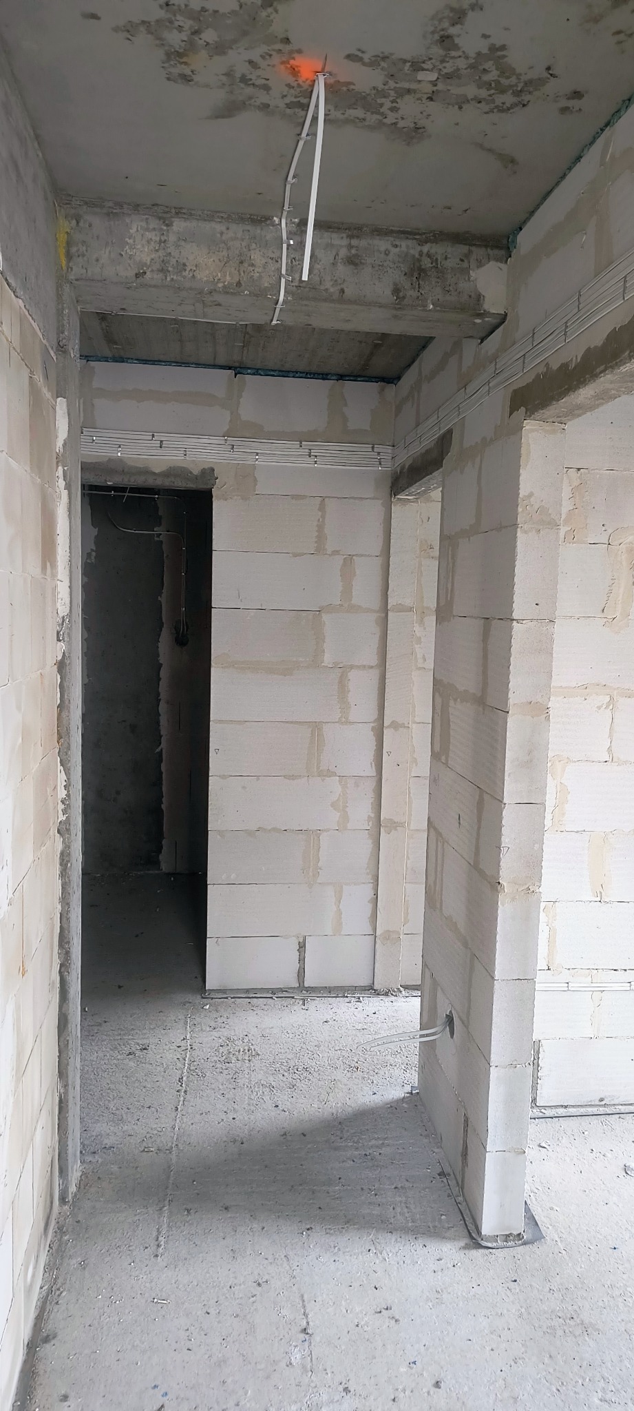 Surowy stan wnętrza z widocznymi przewodami elektrycznymi na suficie i ścianach, w trakcie instalacji w budynku z białych bloczków.