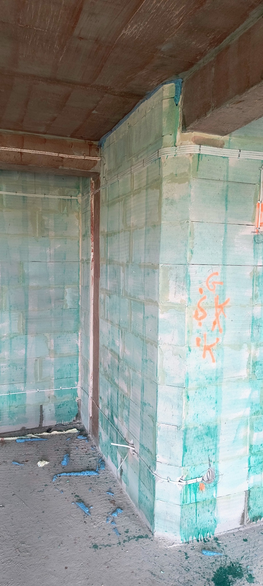 Wnętrze w stanie surowym z widocznymi przewodami elektrycznymi na ścianach z betonu komórkowego. Widoczne puszki instalacyjne i przewody ułożone wzdłuż ścian.