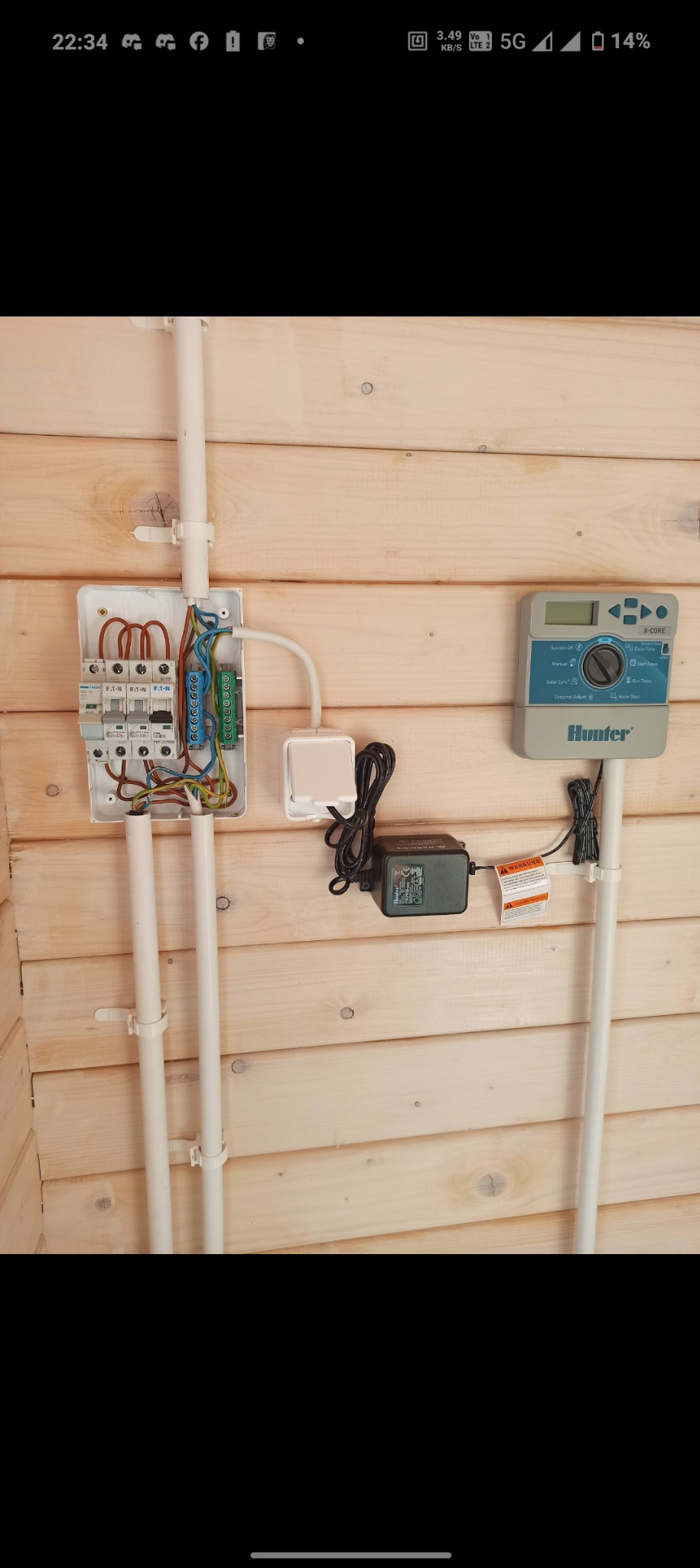 Instalacja elektryczna w drewnianym budynku: rozdzielnica, sterownik nawadniania Hunter X-Core z zasilaczem i okablowaniem.