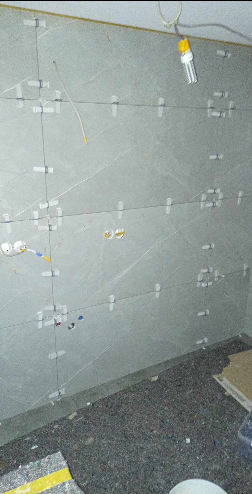 Ściana w trakcie układania szarych płytek w Turośli, widoczne krzyżyki dystansowe, przewody elektryczne i niedokończone gniazdka.