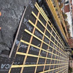 Dastin Burzyński - Konstrukcja drewniana dachu z membraną hydroizolacyjną MONTICA, widoczna w trakcie budowy w Tczewie, z budynkami w tle.