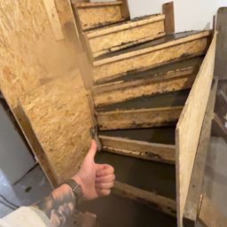 Dastin Burzyński - Wypełnione betonem szalunki schodów wewnętrznych z widoczną dłonią z tatuażem, kciuk w górę.