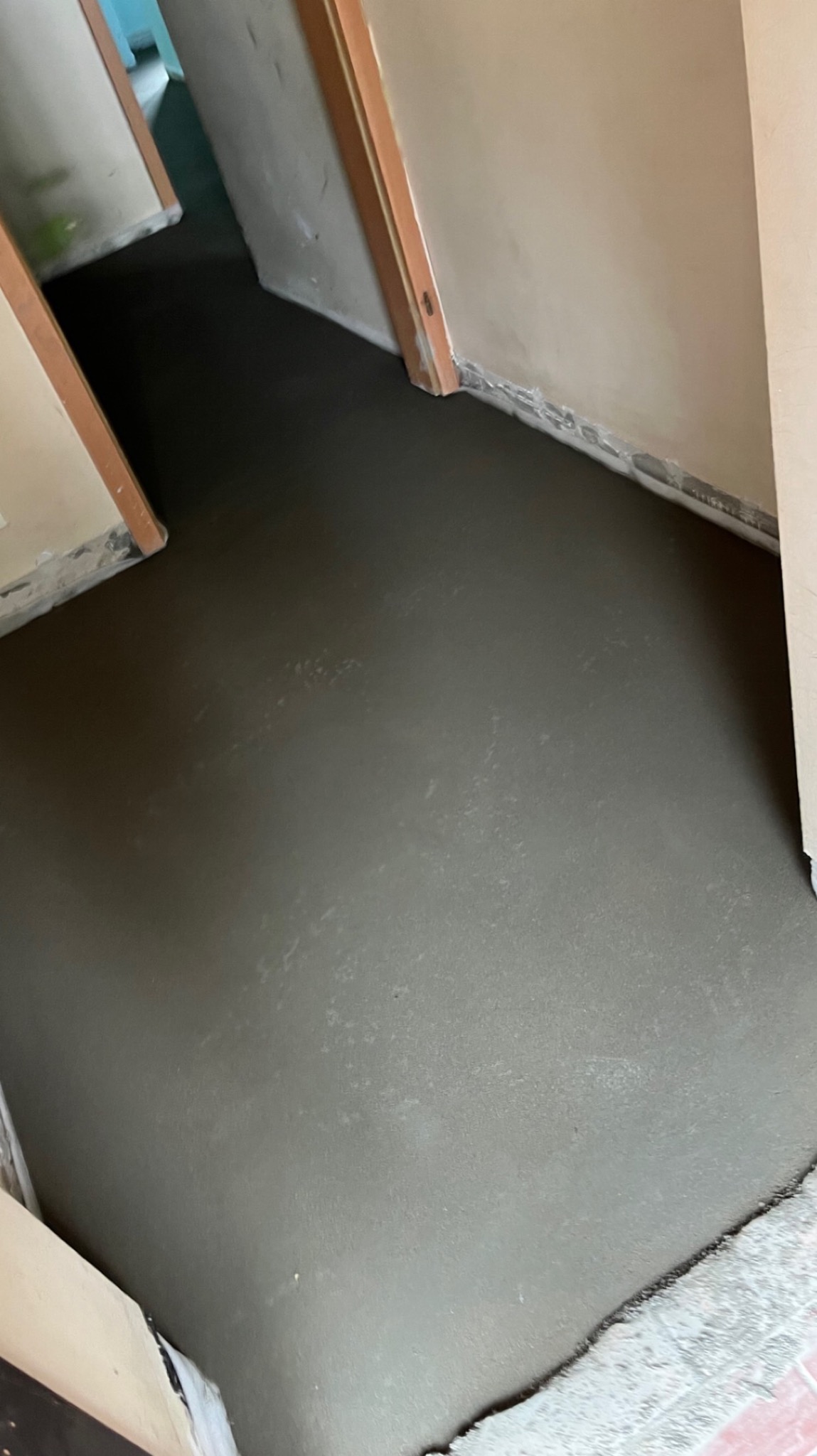 Wylany, świeży podkład podłogowy w korytarzu, zabezpieczone folią ściany przy podłodze.