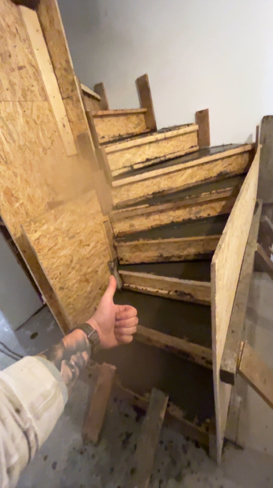 Wypełnione betonem szalunki schodów wewnętrznych z widoczną dłonią z tatuażem, kciuk w górę.