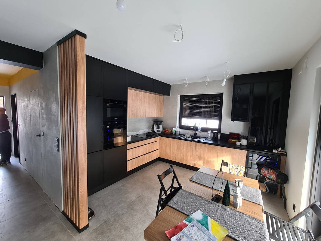 Nowoczesna kuchnia z drewnianymi i czarnymi frontami, widoczny stół z dekoracjami oraz drewniana kolumna dekoracyjna oddzielająca przestrzeń.