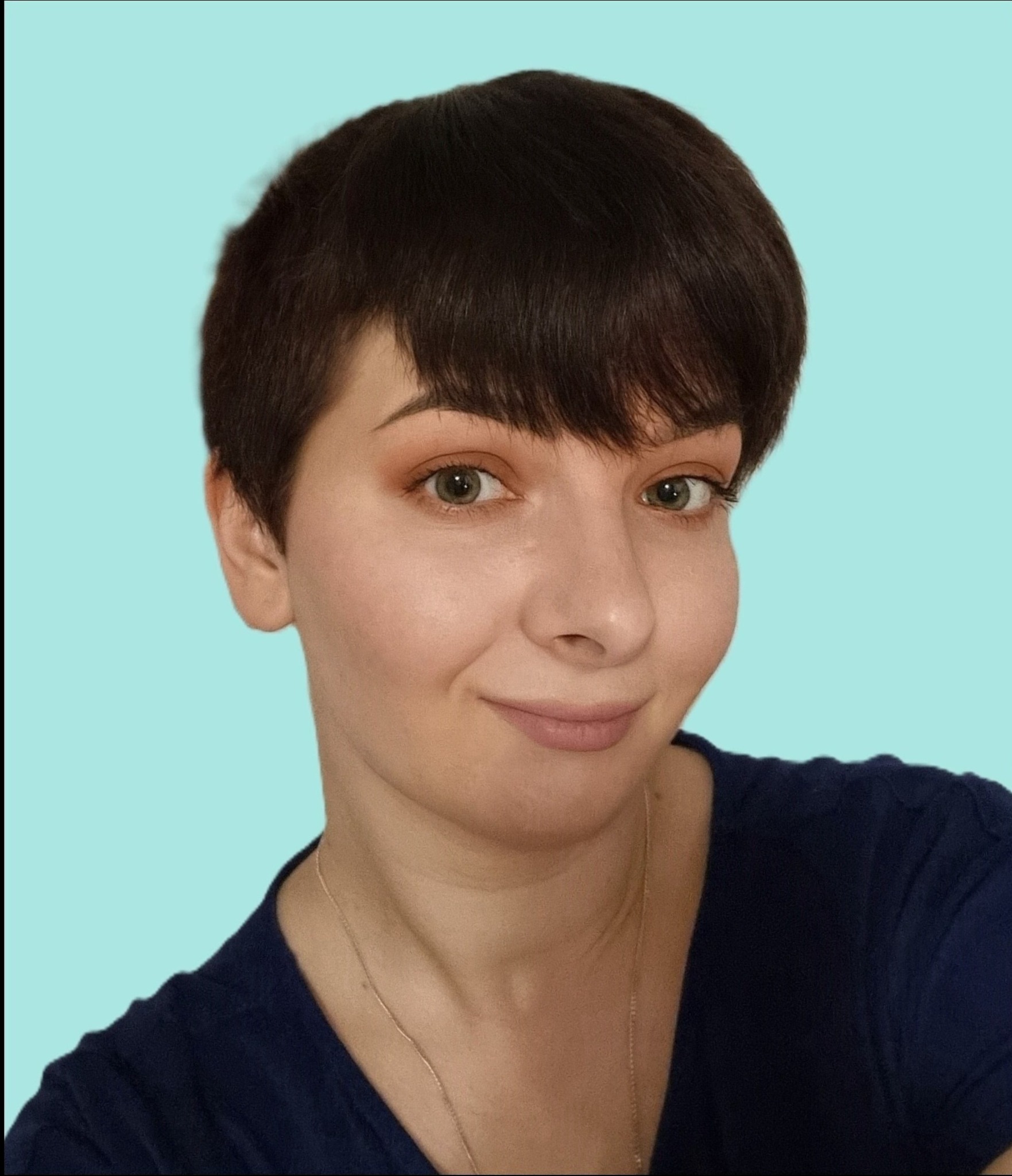 Portret kobiety z krótkimi, ciemnymi włosami, delikatnym makijażem oczu i subtelnym uśmiechem na tle turkusowej ściany.
