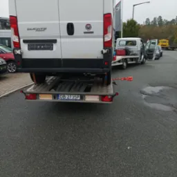 Biały Fiat Ducato Maxi częściowo załadowany na przyczepę lawety, widok z tyłu, tablica rejestracyjna DB 2735P, pomarańczowe pasy zabezpieczające na asfalcie.