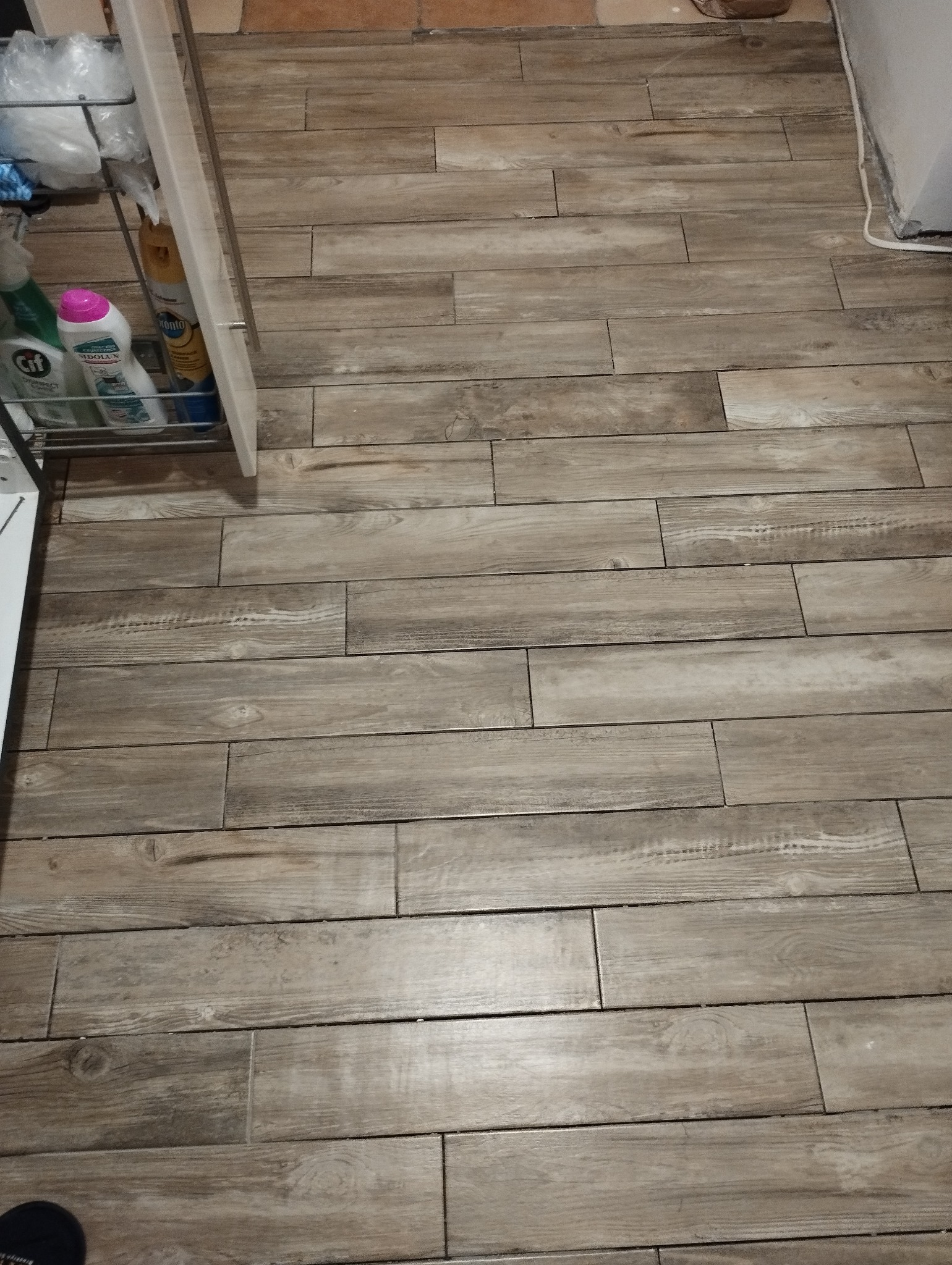 Ułożona podłoga z płytek imitujących drewno, widoczny fragment szafki z chemią gospodarczą.