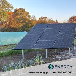S-Energy sp z o.o. - Instalacja paneli słonecznych na gruncie w Wołominie. Widoczne sześć paneli, konstrukcja wsporcza, ogród warzywny w tle i fragment tunelu foliowego.