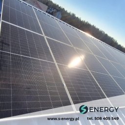 S-Energy sp z o.o. - Instalacja paneli słonecznych na dachu budynku, z widocznym logo firmy S Energy i adresem strony internetowej w prawym dolnym rogu. Słoneczny dzień.