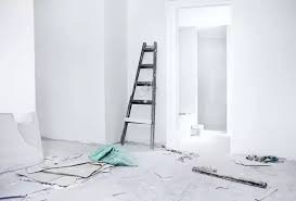 Pomalowane na biało wnętrze w trakcie prac wykończeniowych, drewniana drabina oparta o ścianę, na podłodze resztki materiałów budowlanych i narzędzia.