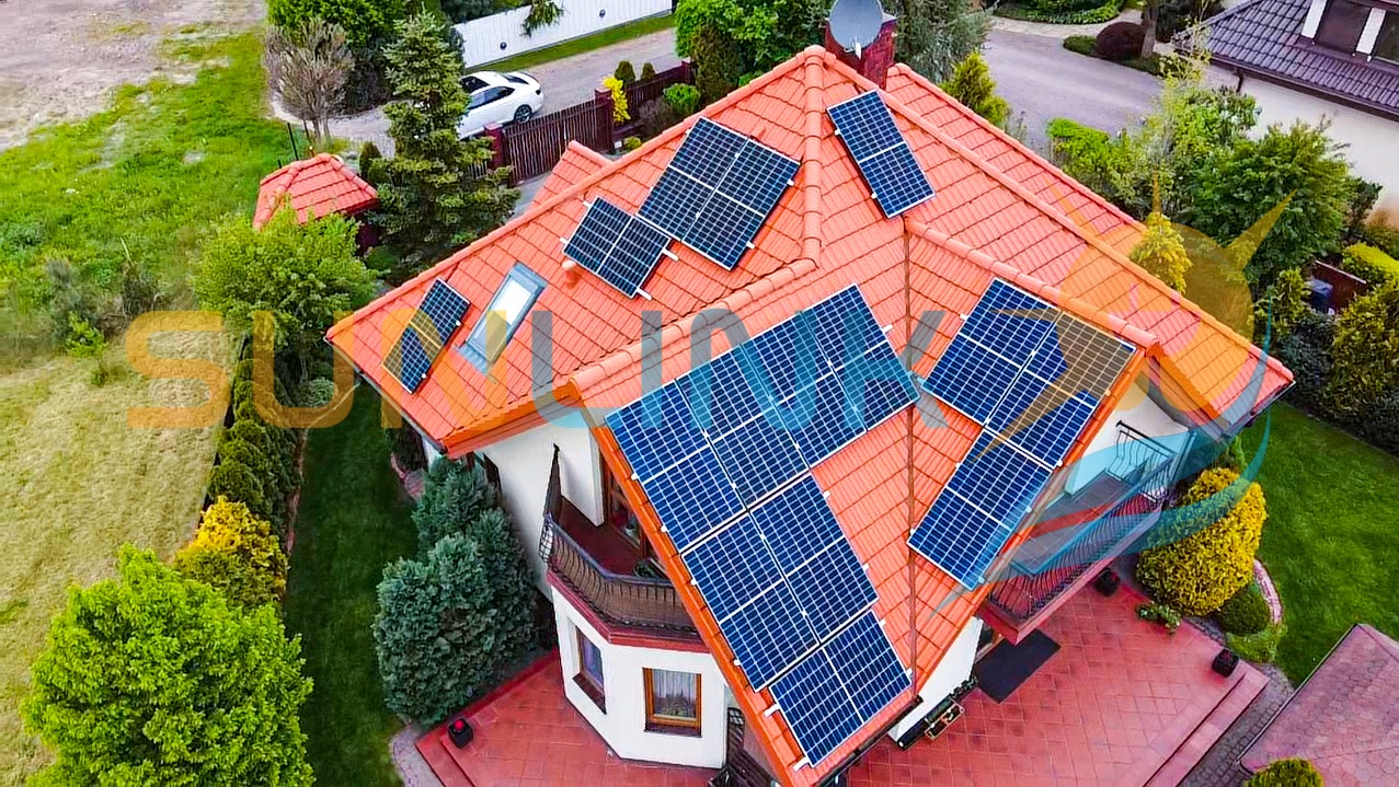 Czerwony dach domu jednorodzinnego z zamontowanymi panelami fotowoltaicznymi, widok z góry, otoczenie zieleni, biały samochód w tle.