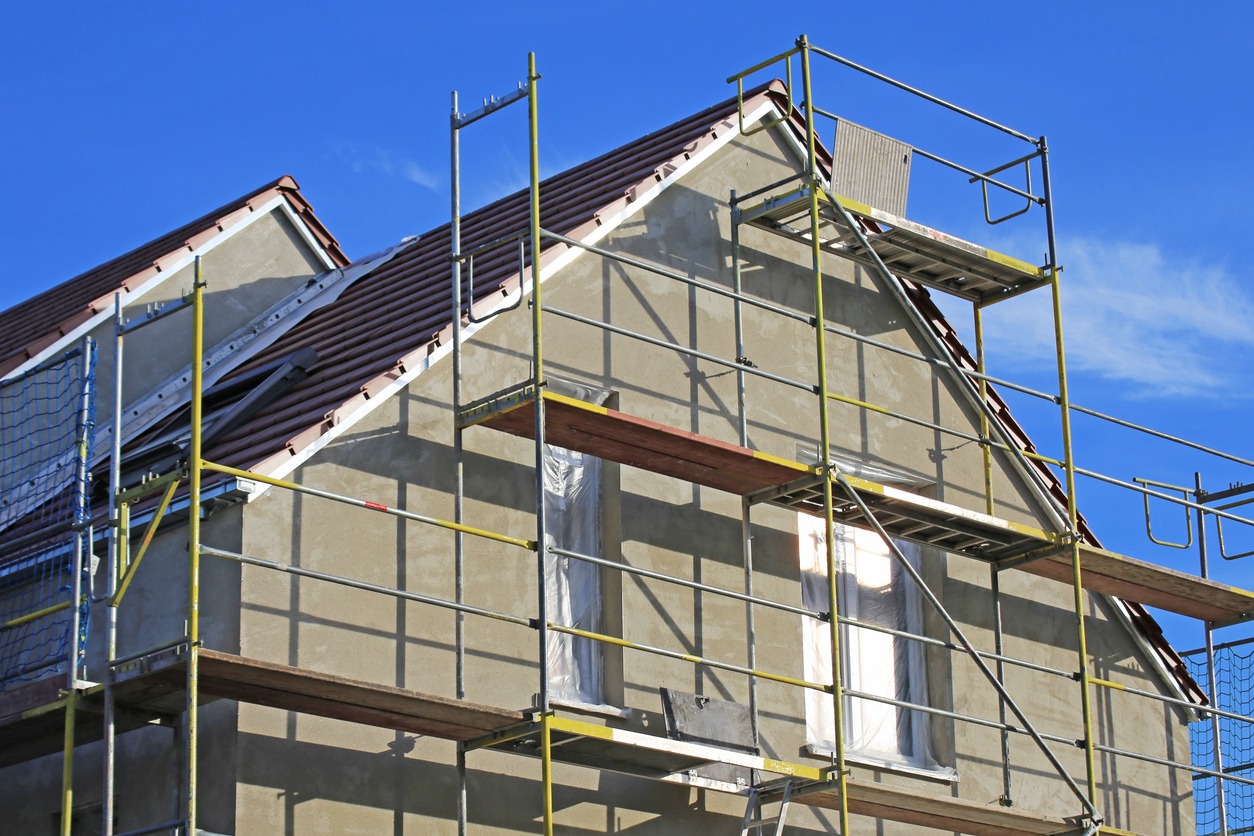 Dom w trakcie nakładania tynku na elewacji, widoczne rusztowania i okna zabezpieczone folią.