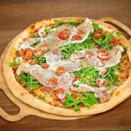 Pizza z szynką parmeńską, rukolą, pomidorkami cherry i parmezanem, podana na drewnianej desce z uchwytami.