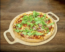 Okrągła pizza z salami, rukolą i ogórkiem konserwowym na drewnianej desce z uchwytami, na tle drewnianego blatu.