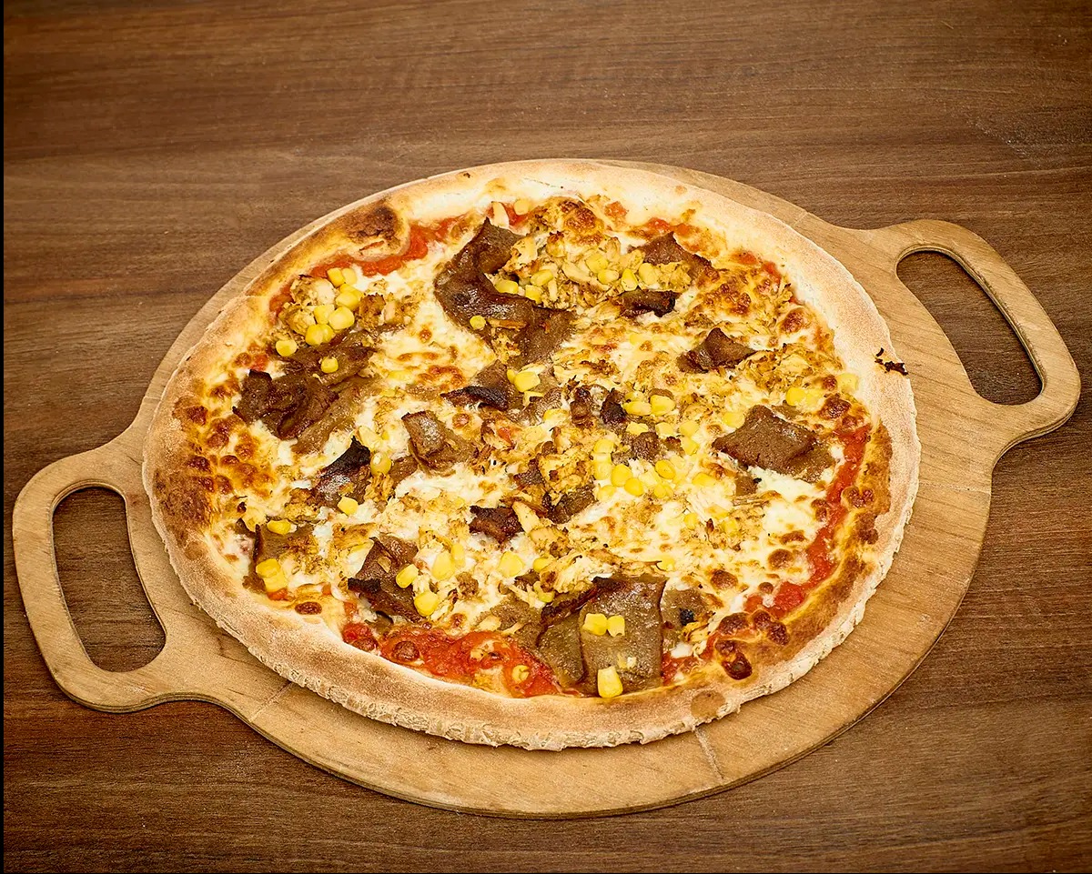 Pizza z mięsem kebab i kukurydzą na drewnianej desce z uchwytami, prezentowana na drewnianym stole.