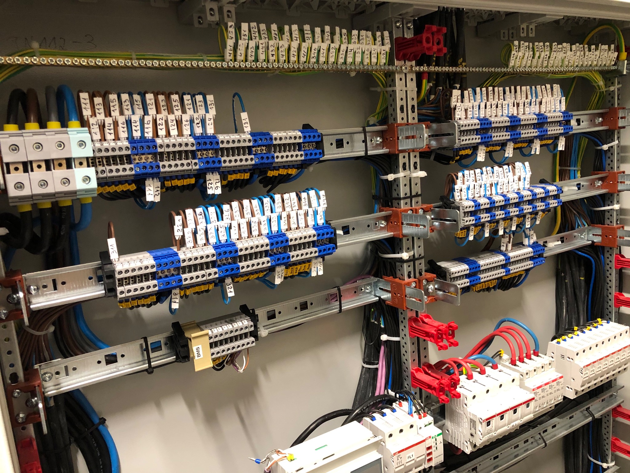 Rozdzielnica elektryczna z zamontowanymi bezpiecznikami, listwami zaciskowymi i okablowaniem, widok z bliska na uporządkowane połączenia.