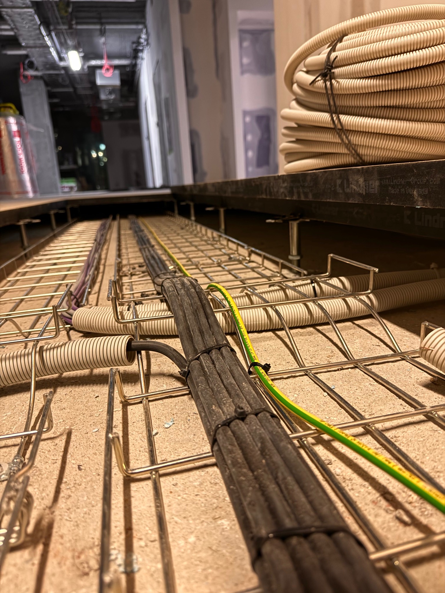 Kable elektryczne prowadzone w metalowej korycie pod podłogą techniczną, widoczne peszle i przewód uziemiający.
