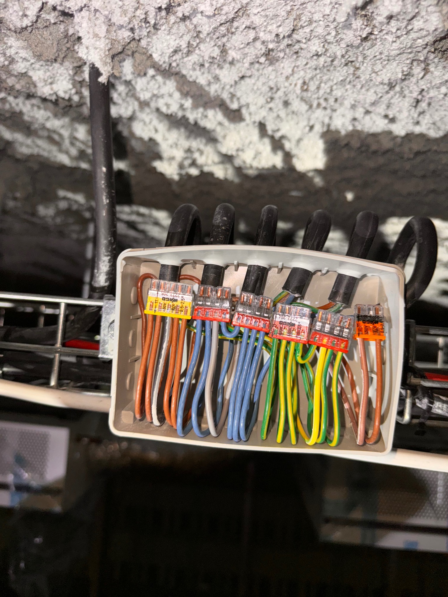 Zestawienie przewodów elektrycznych w puszce instalacyjnej z użyciem szybkozłączek WAGO, widoczne kolory izolacji i oznaczenia złączek, instalacja pod stropem z izolacją natryskową.