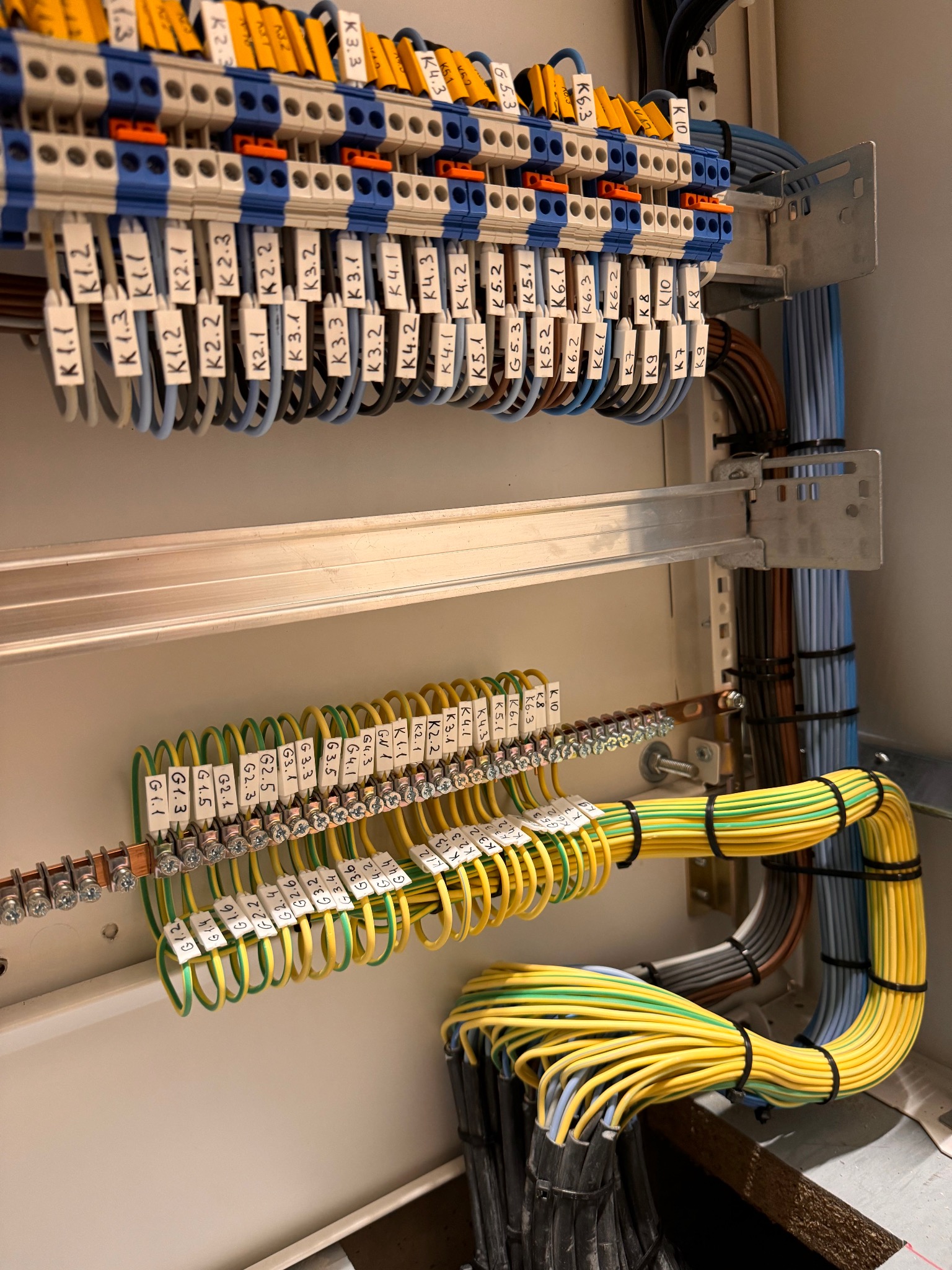 Rozdzielnica elektryczna z precyzyjnie ułożonymi i oznaczonymi przewodami o różnych kolorach, przymocowanymi do listew zaciskowych i szyn DIN.