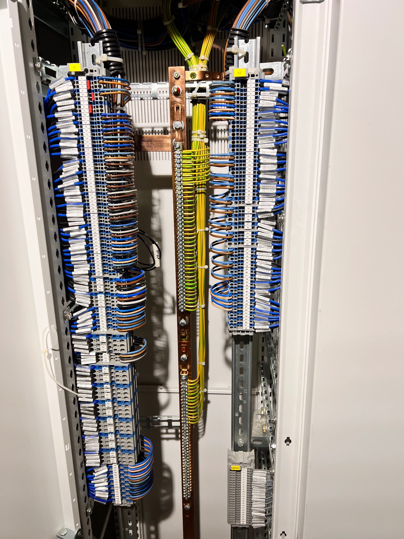 Rozdzielnica elektryczna z precyzyjnie ułożonymi przewodami o różnych kolorach, podłączonymi do listew zaciskowych z etykietami, widoczne szyny DIN i elementy montażowe wewnątrz szafy.