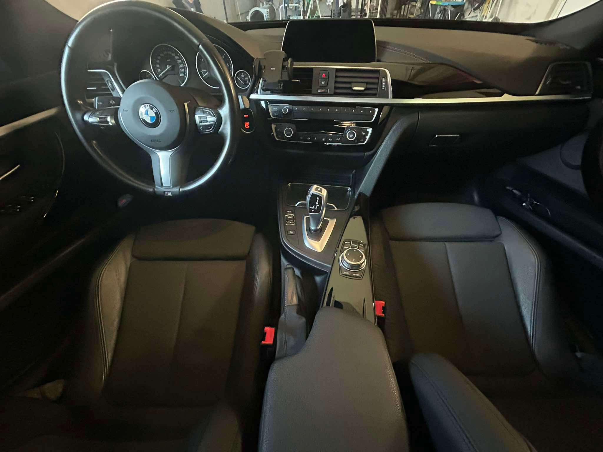 Wnętrze samochodu BMW z czarną skórzaną tapicerką, widok z przodu na deskę rozdzielczą, kierownicę i fotele.