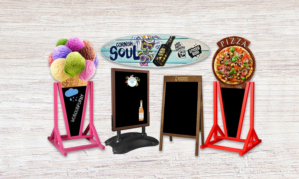 Różnorodne tablice reklamowe: różowa z lodami i napisem 'Wodoodporny', czarna z logo firmy i napojem, drewniana z logo Dunkin' Donuts, czerwona z pizzą, oraz deska surfingowa z napisem 'Cornish...