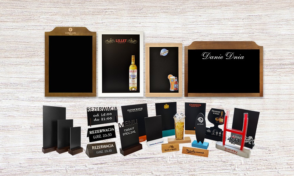 Różnorodne tablice i stojaki z menu, w tym tablice kredowe w drewnianych ramach, tabliczki z rezerwacjami i menu na drewnianych podstawkach, prezentowane na tle drewnianej tekstury.
