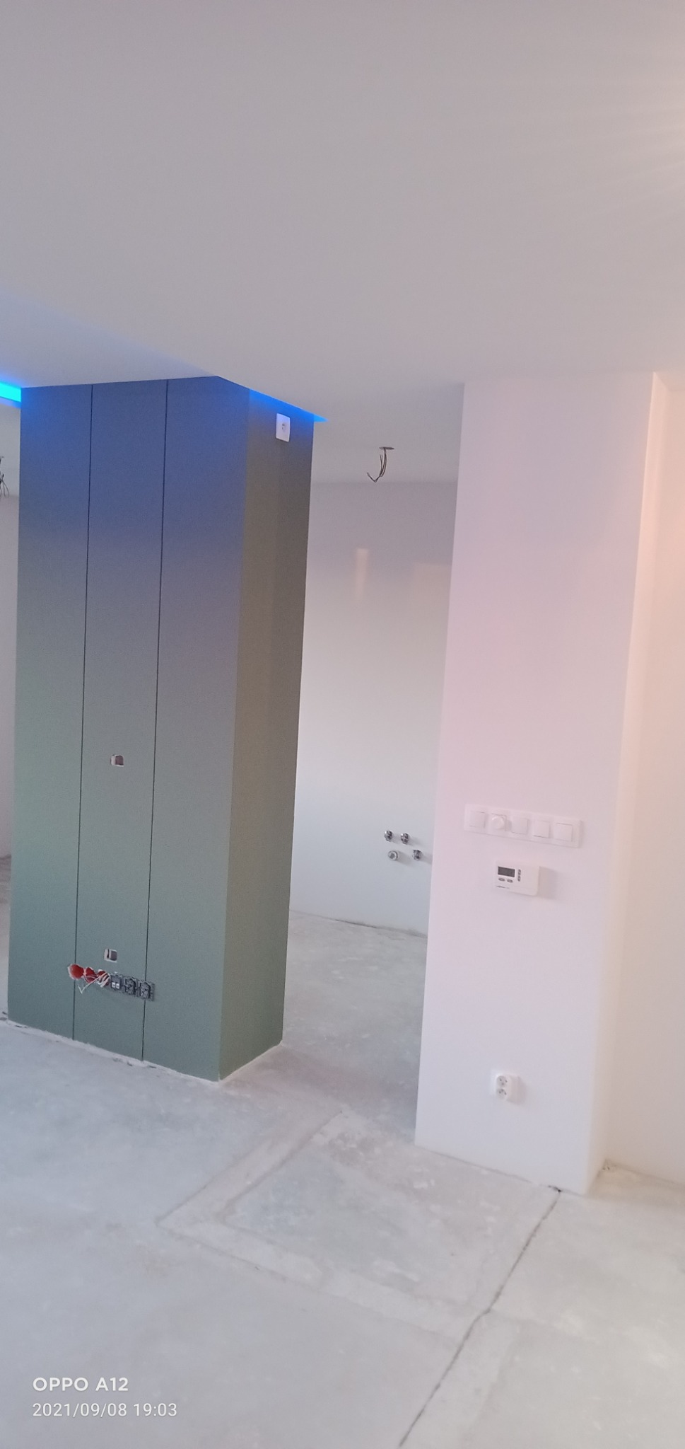 Wnętrze w trakcie prac wykończeniowych: pionowa zabudowa z podświetleniem LED, niezabezpieczone kable elektryczne, surowe ściany i podłoga.