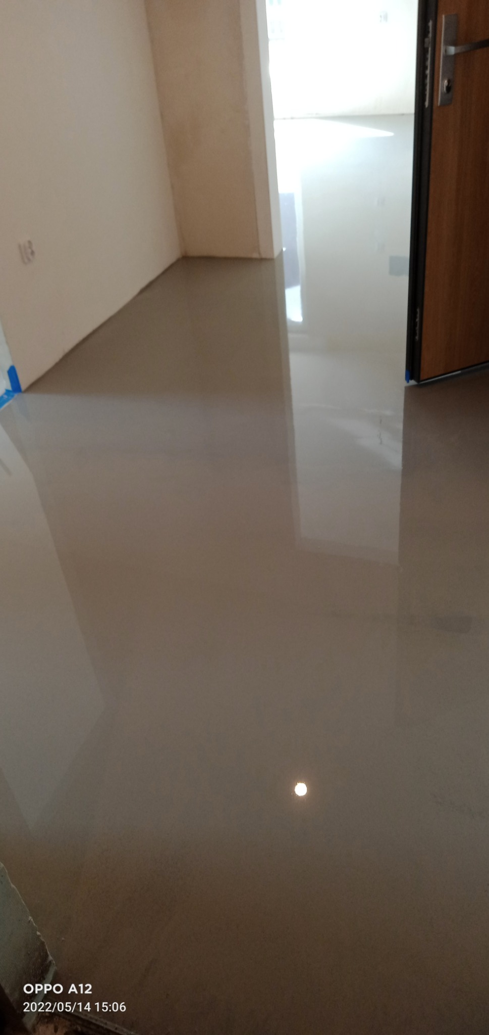 Wypoziomowana, gładka, wylewka samopoziomująca na podłodze w jasnym pomieszczeniu, widoczny fragment ściany z niedokończonymi gładziami i otwarte drzwi.