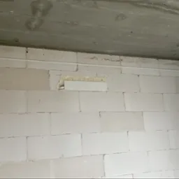 Ściana z białych bloczków z zamontowaną białą listwą maskującą instalację, widoczna szpara wypełniona pianką montażową.