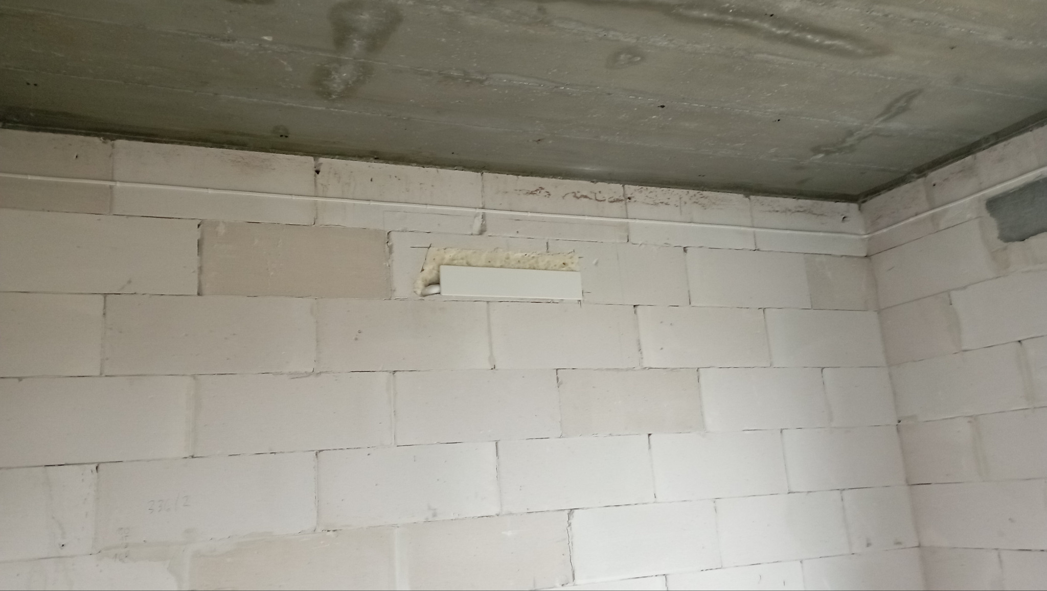 Ściana z białych bloczków z zamontowaną białą listwą maskującą instalację, widoczna szpara wypełniona pianką montażową.