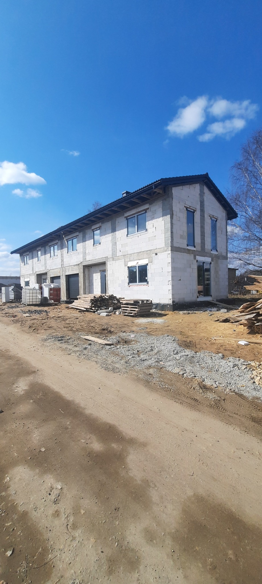 Budynek w stanie surowym otwartym z zamontowanymi oknami i drzwiami, widoczne materiały budowlane i plac budowy.