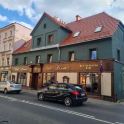 Odnowiona fasada kamienicy z szyldem 'Pub Lissa' i 'Restauracja Bar', z nową elewacją w kolorze zieleni i brązu, widok z ulicy, samochody na pierwszym planie.