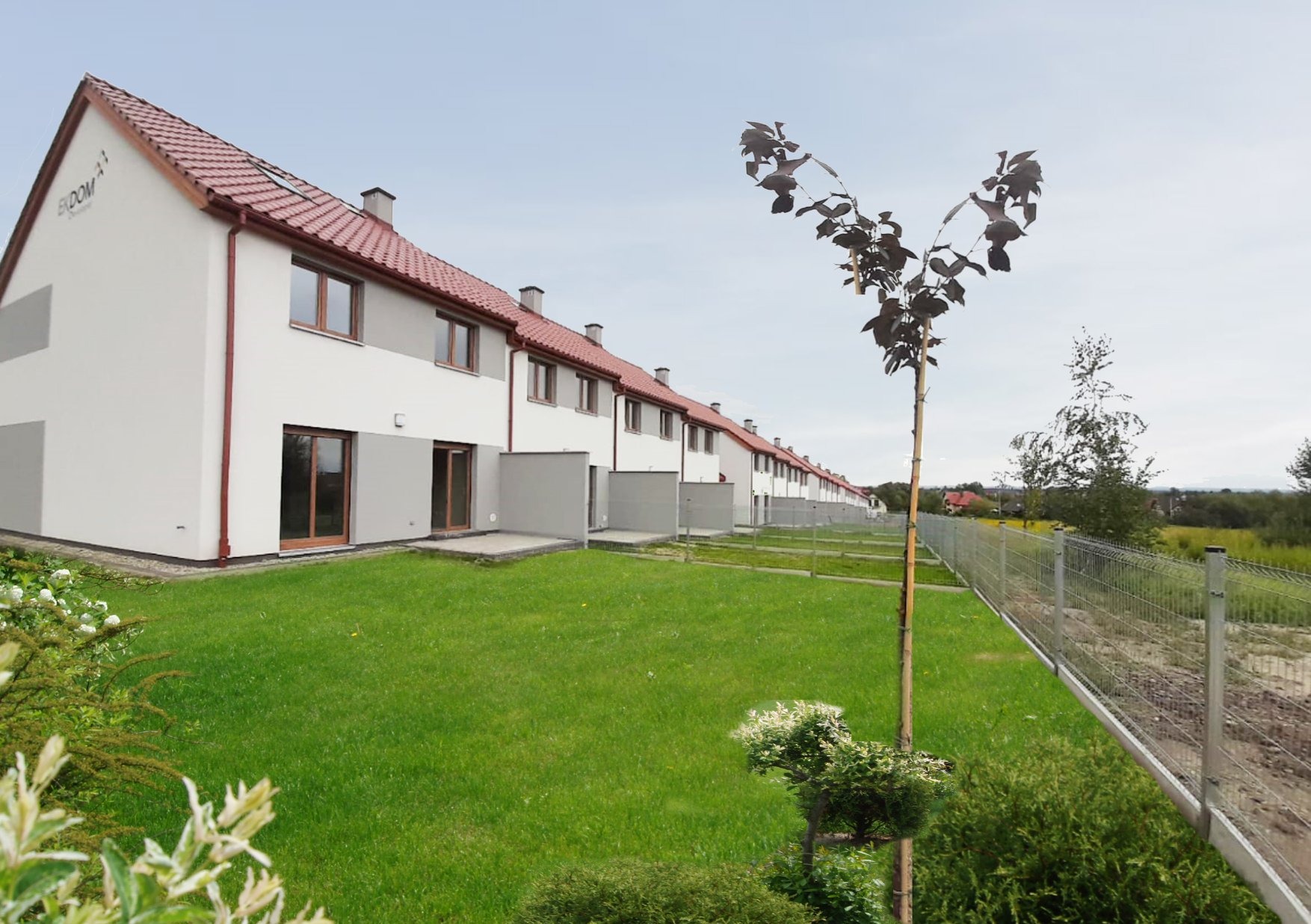 Szereg identycznych, dwukondygnacyjnych domów z czerwonymi dachami, białymi ścianami i drewnianymi oknami, widziane z perspektywy ogrodu.