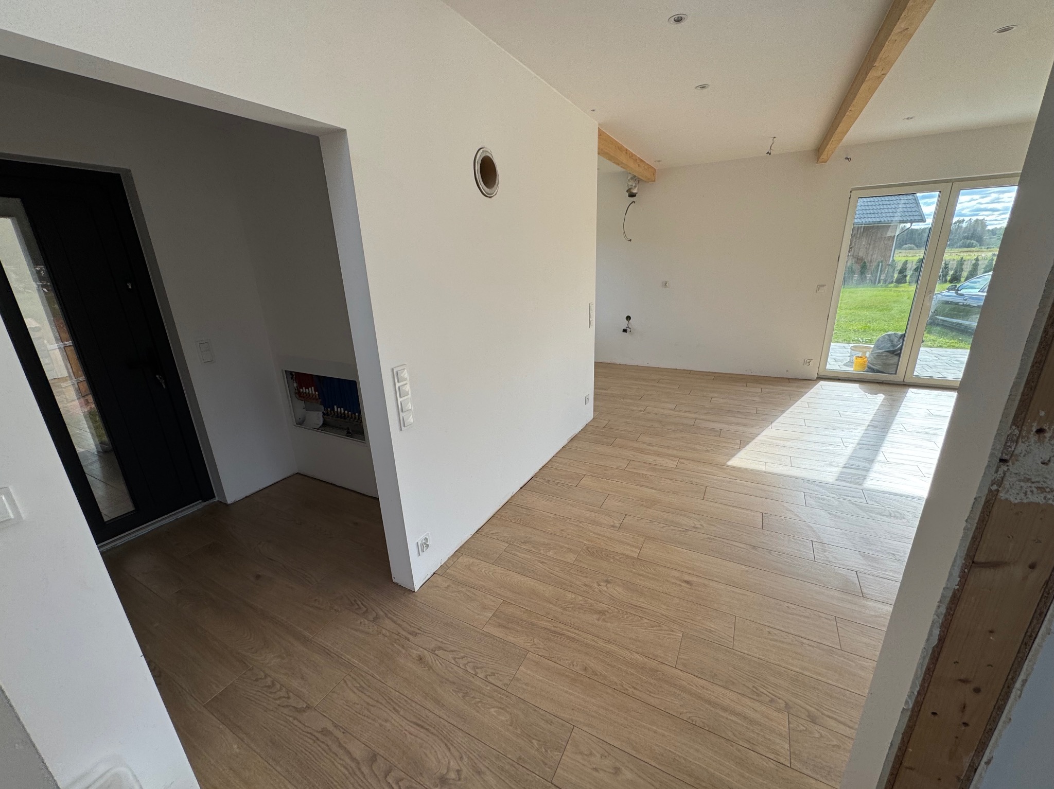 Jasne panele podłogowe ułożone w nowym, przestronnym wnętrzu z białymi ścianami i drewnianymi belkami stropowymi. Widoczne przygotowania do dalszych prac wykończeniowych.