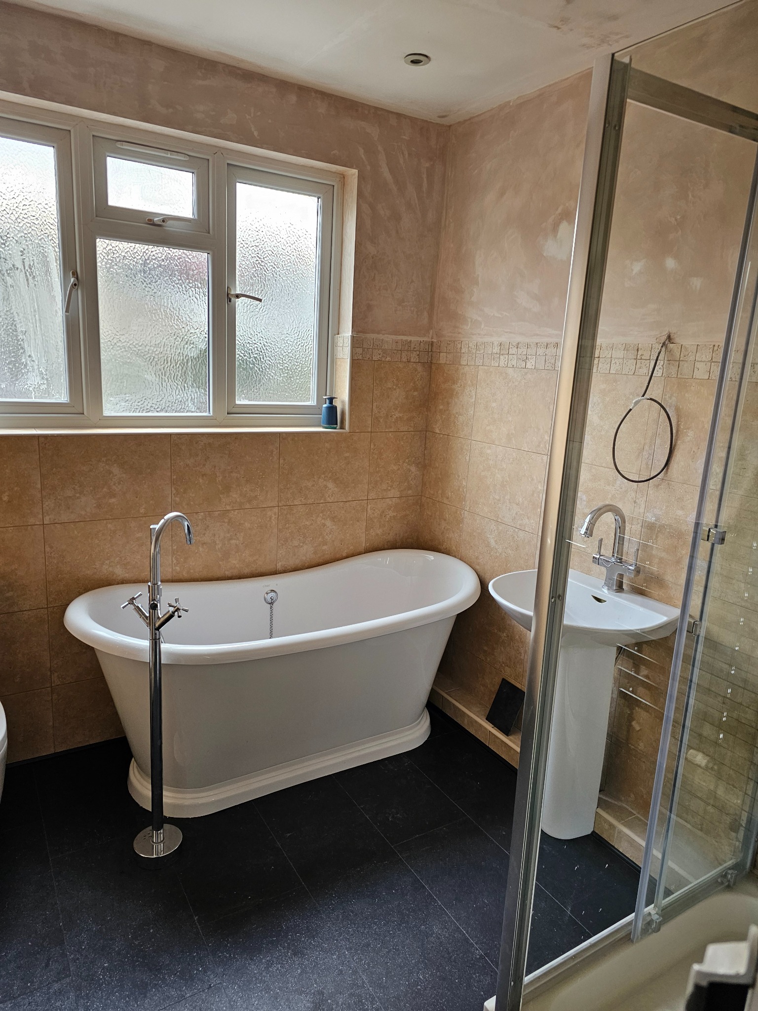 Łazienka w trakcie remontu: ściany po szpachlowaniu, widoczna wanna wolnostojąca z chromowaną baterią, umywalka na postumencie i kabina prysznicowa z widocznymi śladami użytkowania.