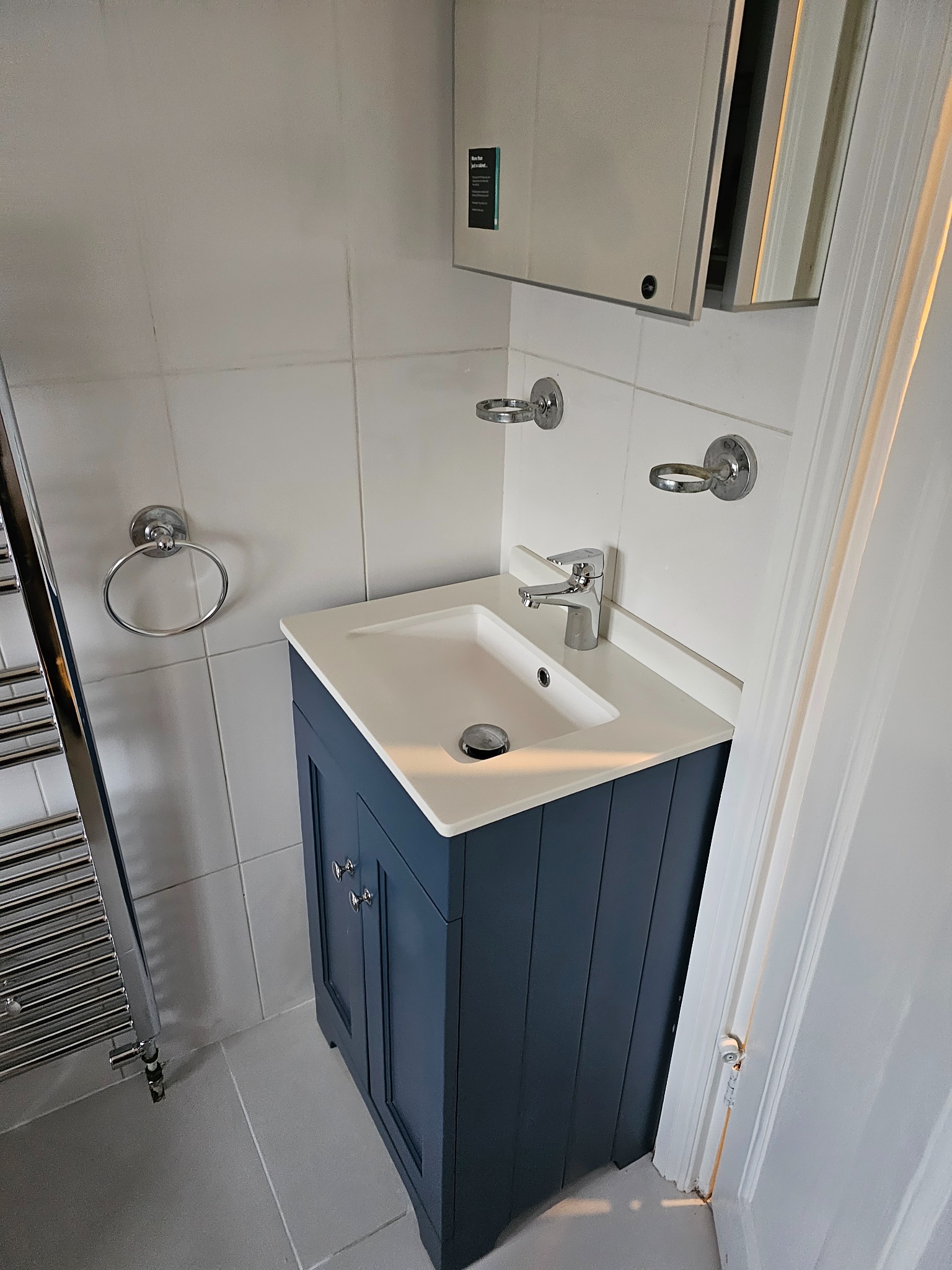Nowoczesna łazienka w Janowie Podlaskim po remoncie: umywalka z szafką w kolorze granatowym, biały blat, bateria chromowana, grzejnik drabinkowy i lustro z szafką.