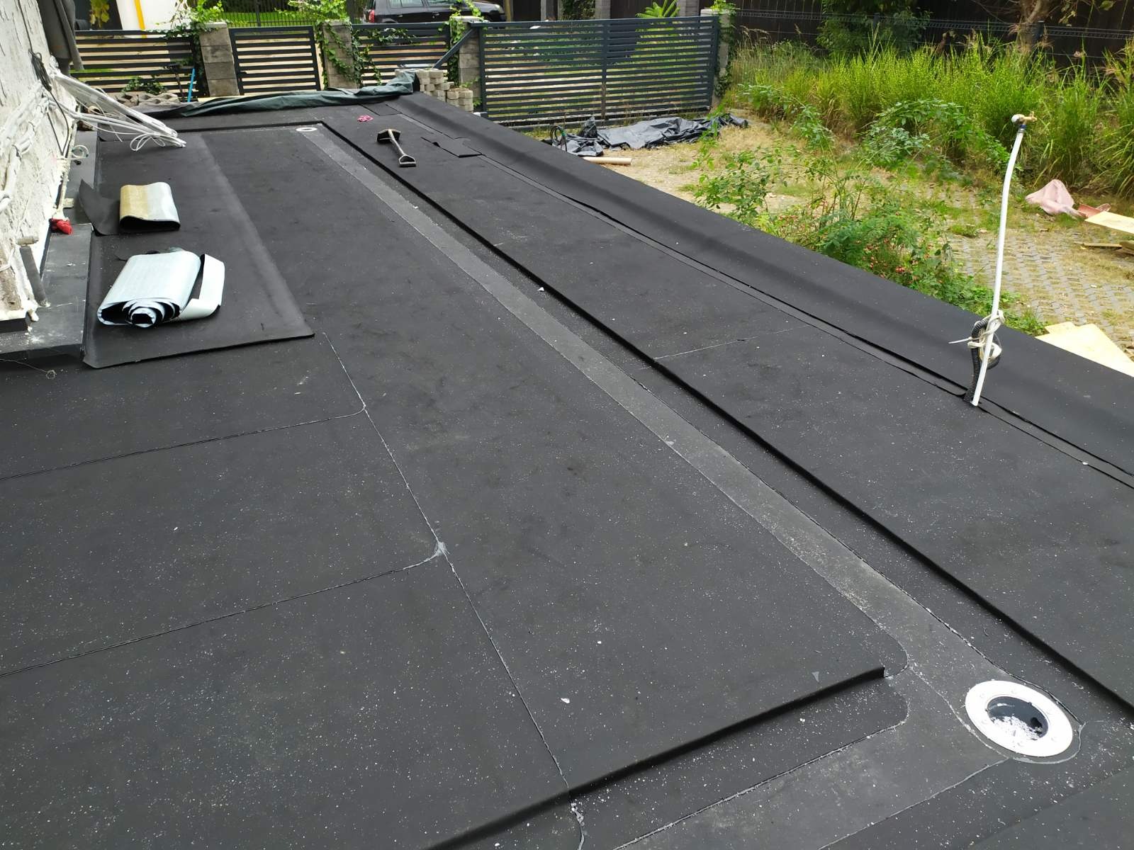 Czarny, płaski dach pokryty papą termozgrzewalną z widocznym kominkiem odpowietrzającym i fragmentami zwiniętej membrany na powierzchni.