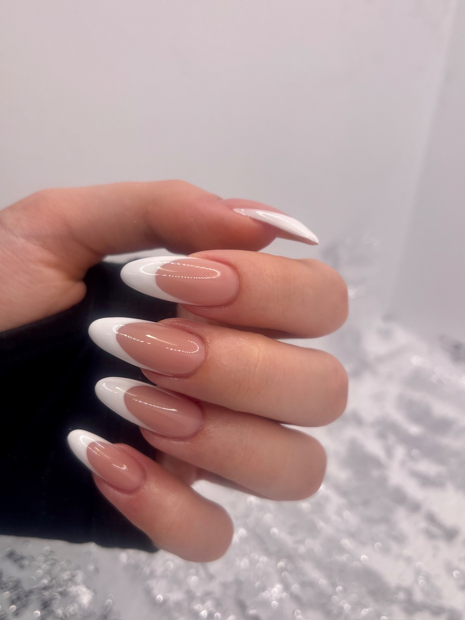 Dłoń z perfekcyjnym manicure francuskim w Legionowie, z owalnymi paznokciami i idealnie białymi końcówkami na tle srebrzystego, błyszczącego podłoża.