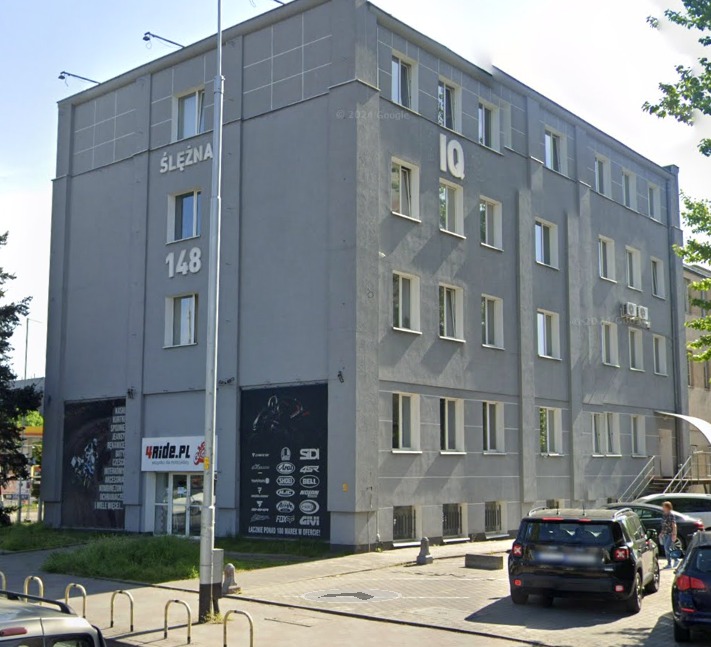 Szary budynek biurowy z napisem 'Ślężna 148' i logo 'IQ' na fasadzie, z reklamami sklepów motocyklowych na parterze.
