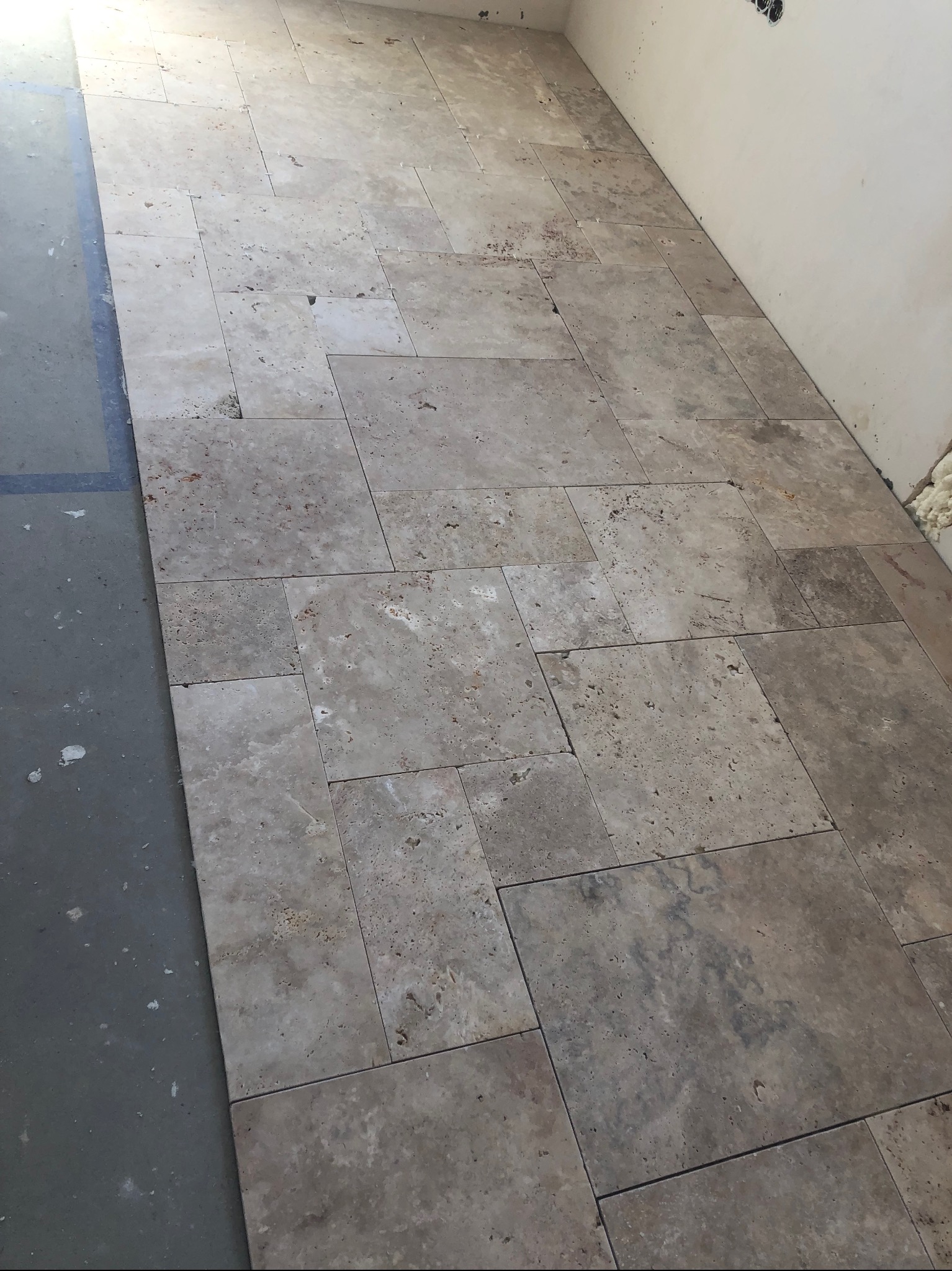 Ułożona podłoga z trawertynu w nieregularnym wzorze, widoczne fragmenty surowego betonu i ściany z pianką montażową.