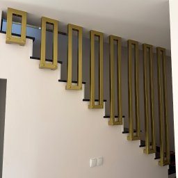 Mat-Spaw Mateusz Nóżka - Nowoczesne schody z oryginalną, złotą balustradą o geometrycznym wzorze, widok z dołu. Minimalistyczny design w jasnym wnętrzu.