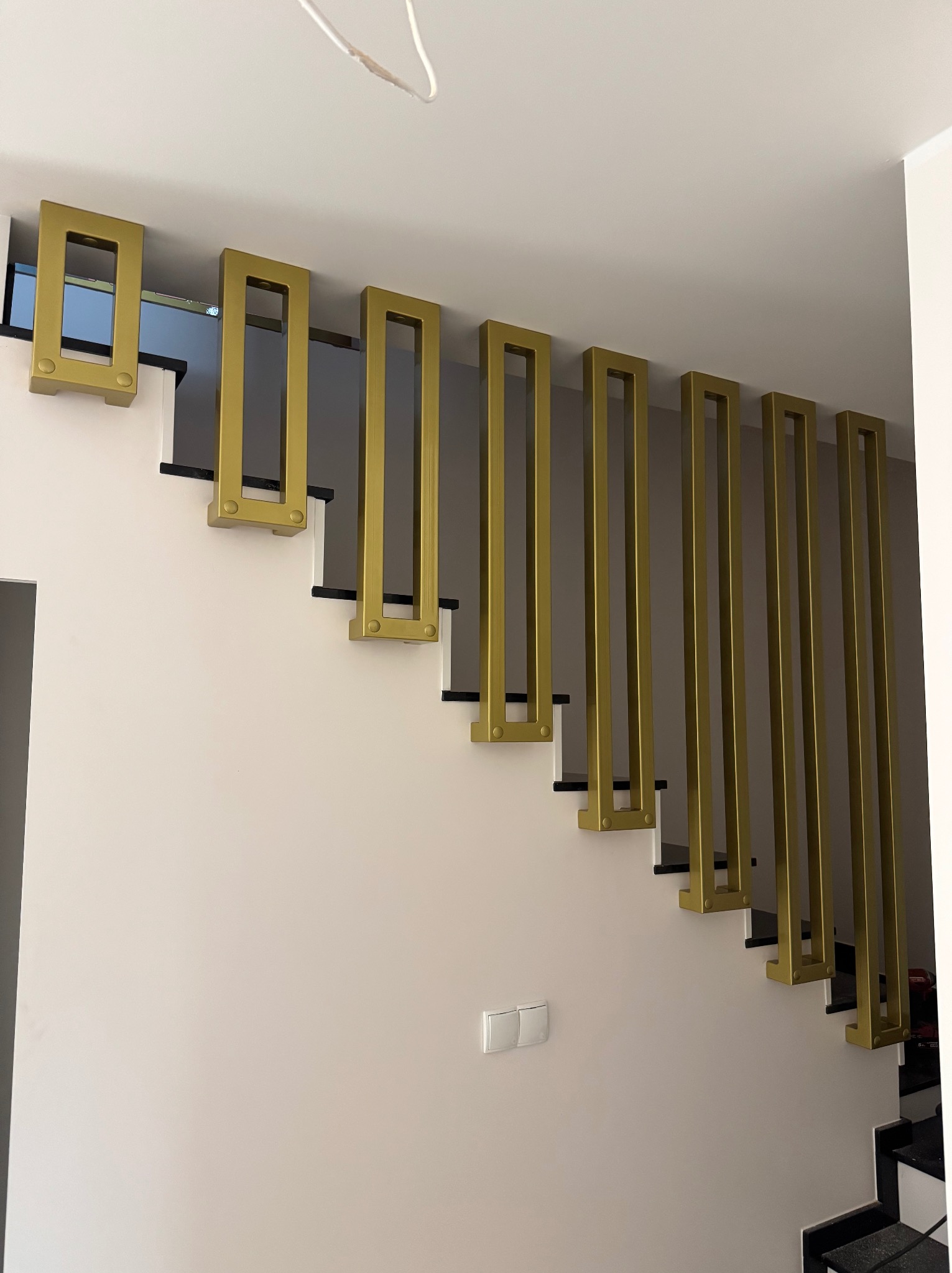 Nowoczesne schody z oryginalną, złotą balustradą o geometrycznym wzorze, widok z dołu. Minimalistyczny design w jasnym wnętrzu.