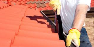 Dekarz w żółtych rękawicach montuje rynnę na dachu pokrytym czerwoną dachówką.